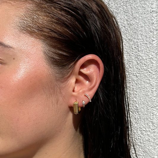 A female model with brunette hair wearing the 18K Gold Filled Grooved C-Hoop Earrings shown from a side angle