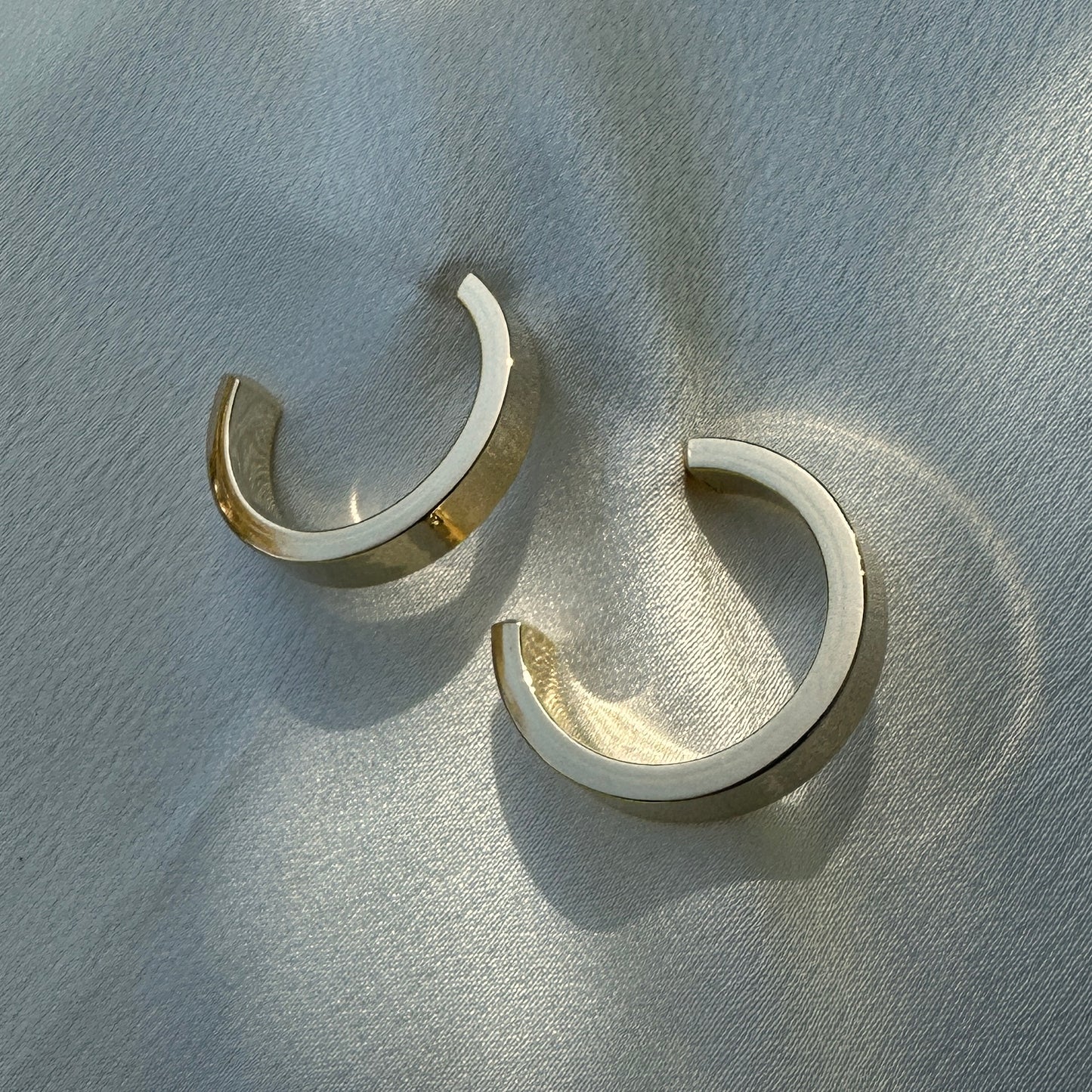A close up product image of the 18K Gold Filled Sleek Semi Hoop Earrings displayed on white satin fabric