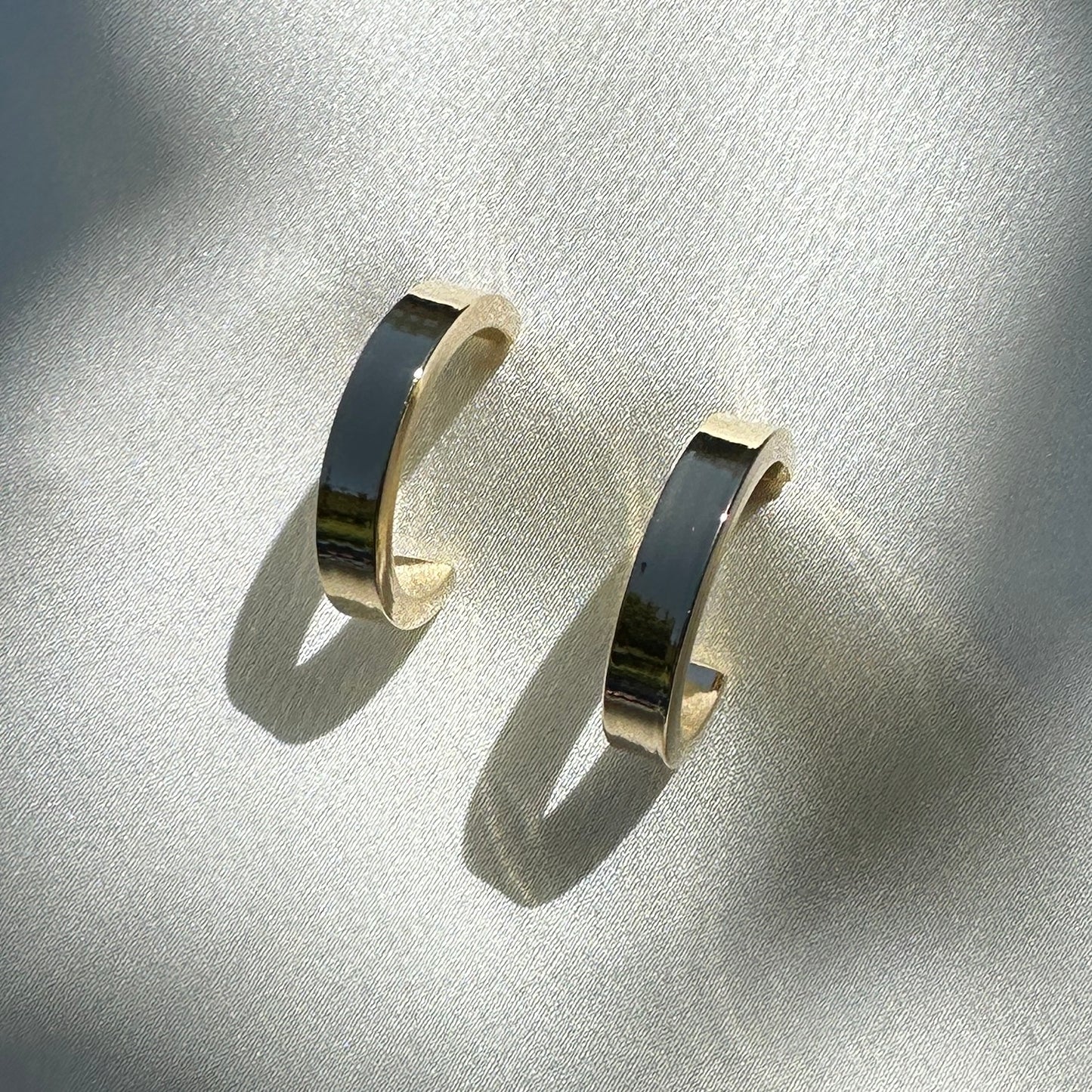 A close up product image of the 18K Gold Filled Sleek Semi Hoop Earrings displayed on white satin fabric shown from a front angle