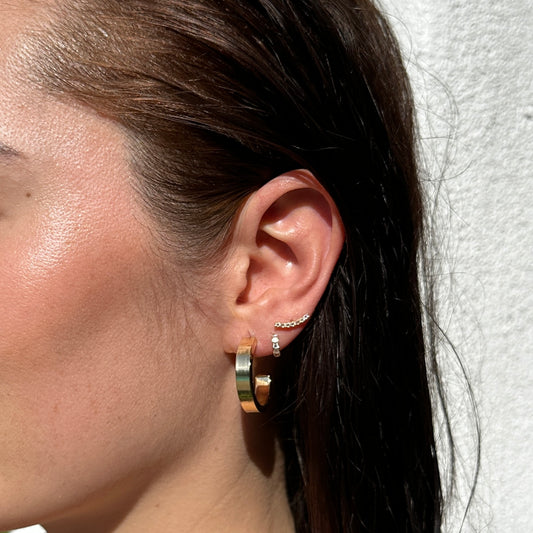 A close up of a female model with brunette hair wearing the 18K Gold Filled Sleek Semi Hoop Earrings