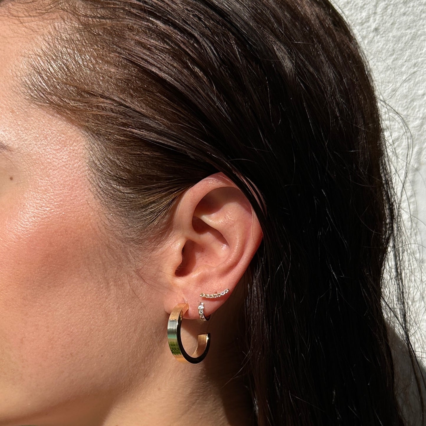 A close up image of a female model's ear wearing the 18K Gold Filled Sleek Semi Hoop Earrings