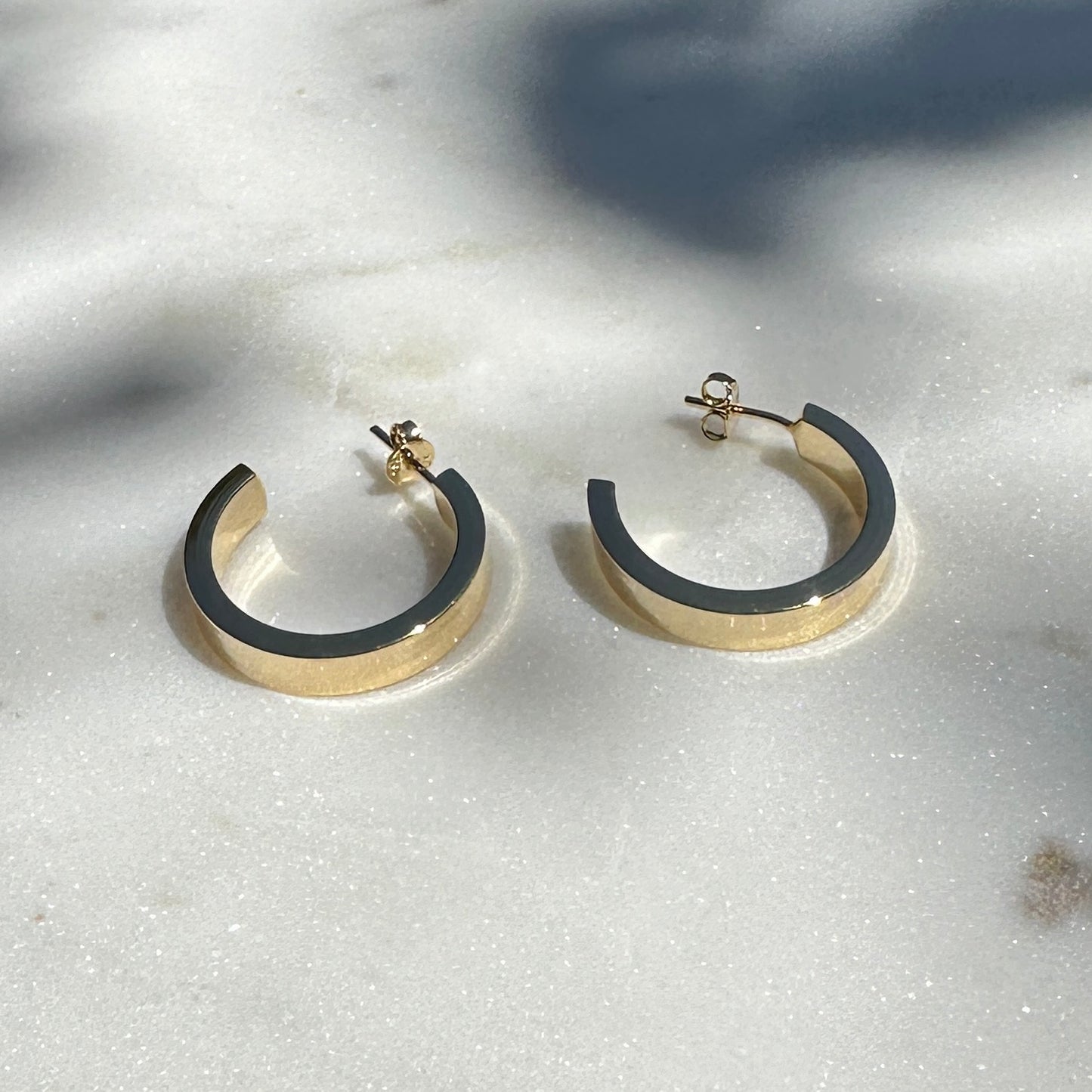 A close up product image of the 18K Gold Filled Sleek Semi Hoop Earrings displayed on white satin fabric shown from a side angle