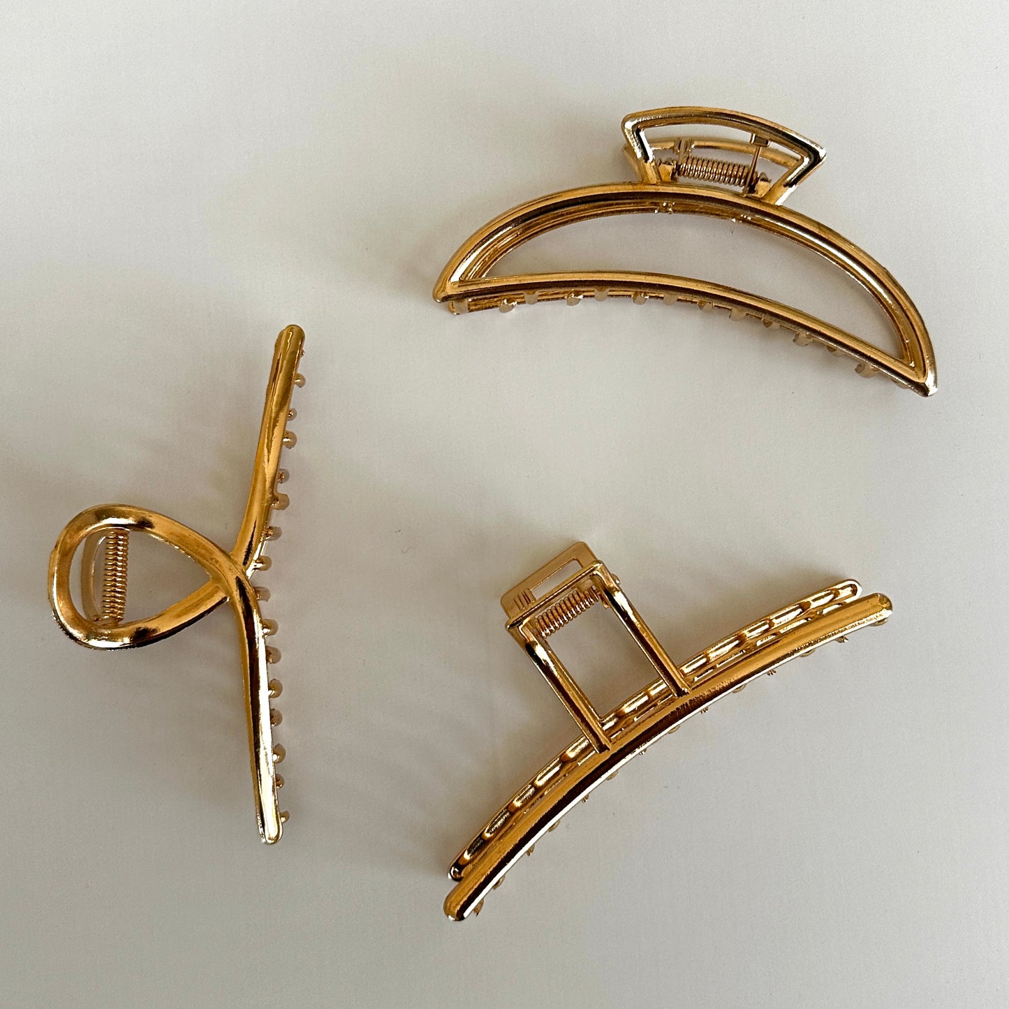 A close up product image showing 3 different Gold-Tone Metal Hair Claw Clip styles including Loop, Minimal, and Crescent