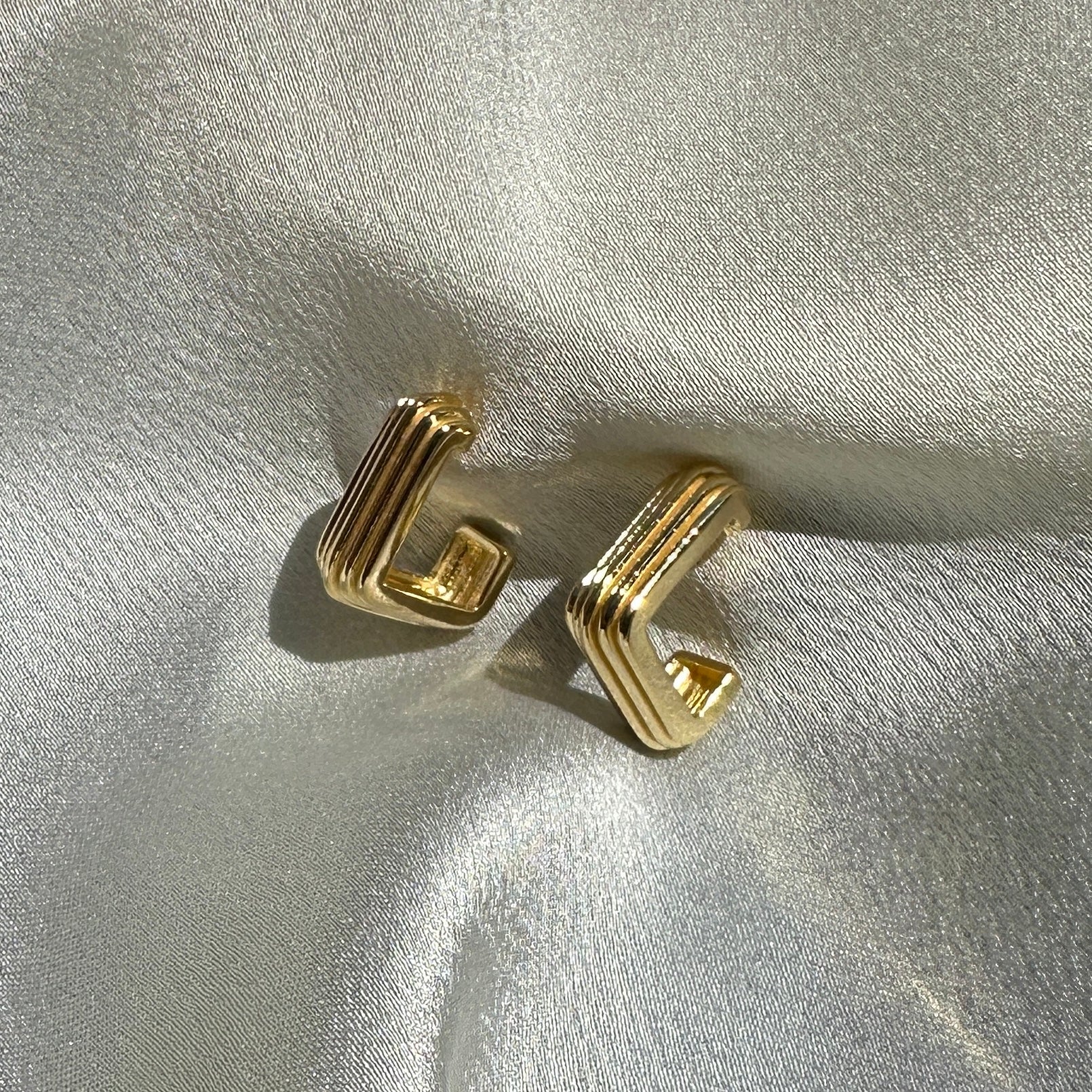A close up product image of the 18K Gold Filled Grooved C-Hoop Earrings displayed on white satin fabric