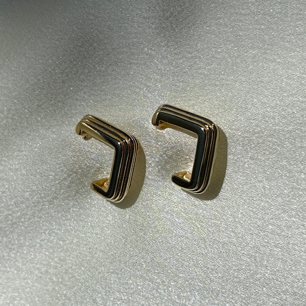 A close up product image of the 18K Gold Filled Grooved C-Hoop Earrings from a side angle displayed on white satin fabric