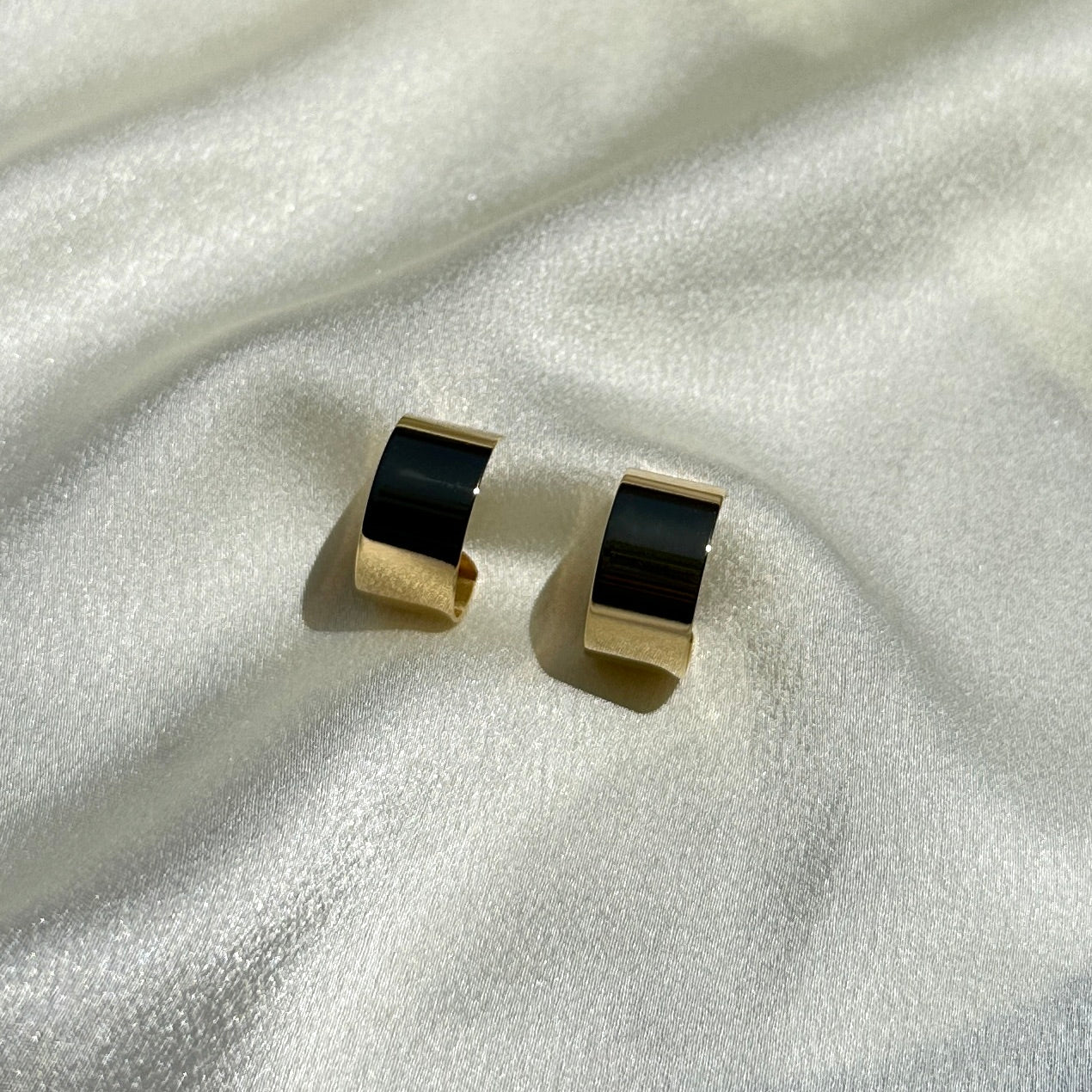 A pair of the 18K Gold Filled Thin Wide Polished Semi Hoop Earrings on shiny fabric displayed from front angle