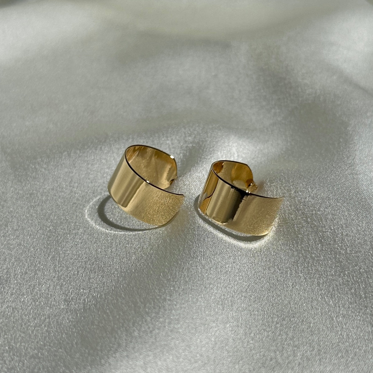 A pair of the 18K Gold Filled Thin Wide Polished Semi Hoop Earrings on shiny fabric displayed from side angle 
