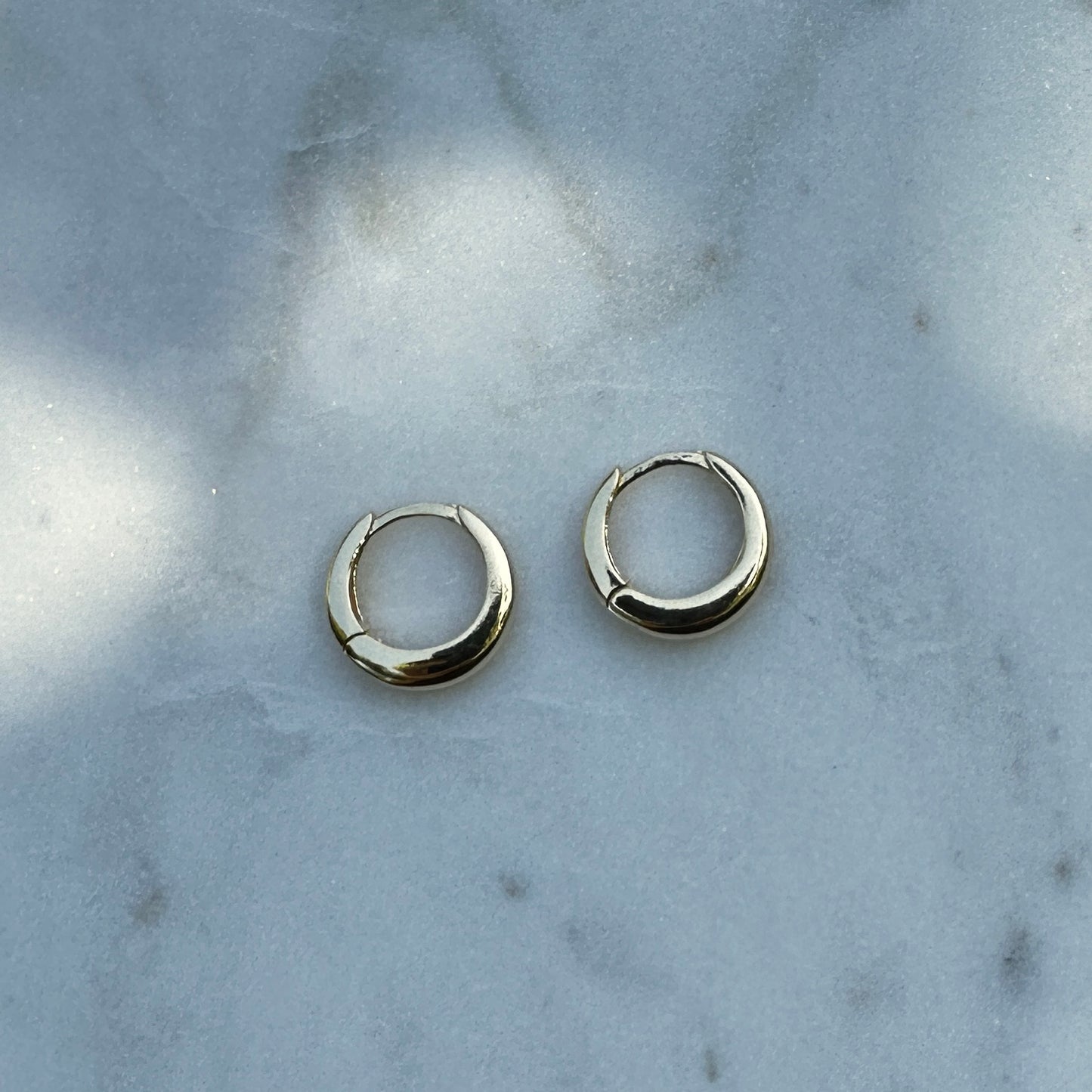 A pair of the 18K Gold Filled Classic Clicker Hoop Earrings on white marble surface from above angle 