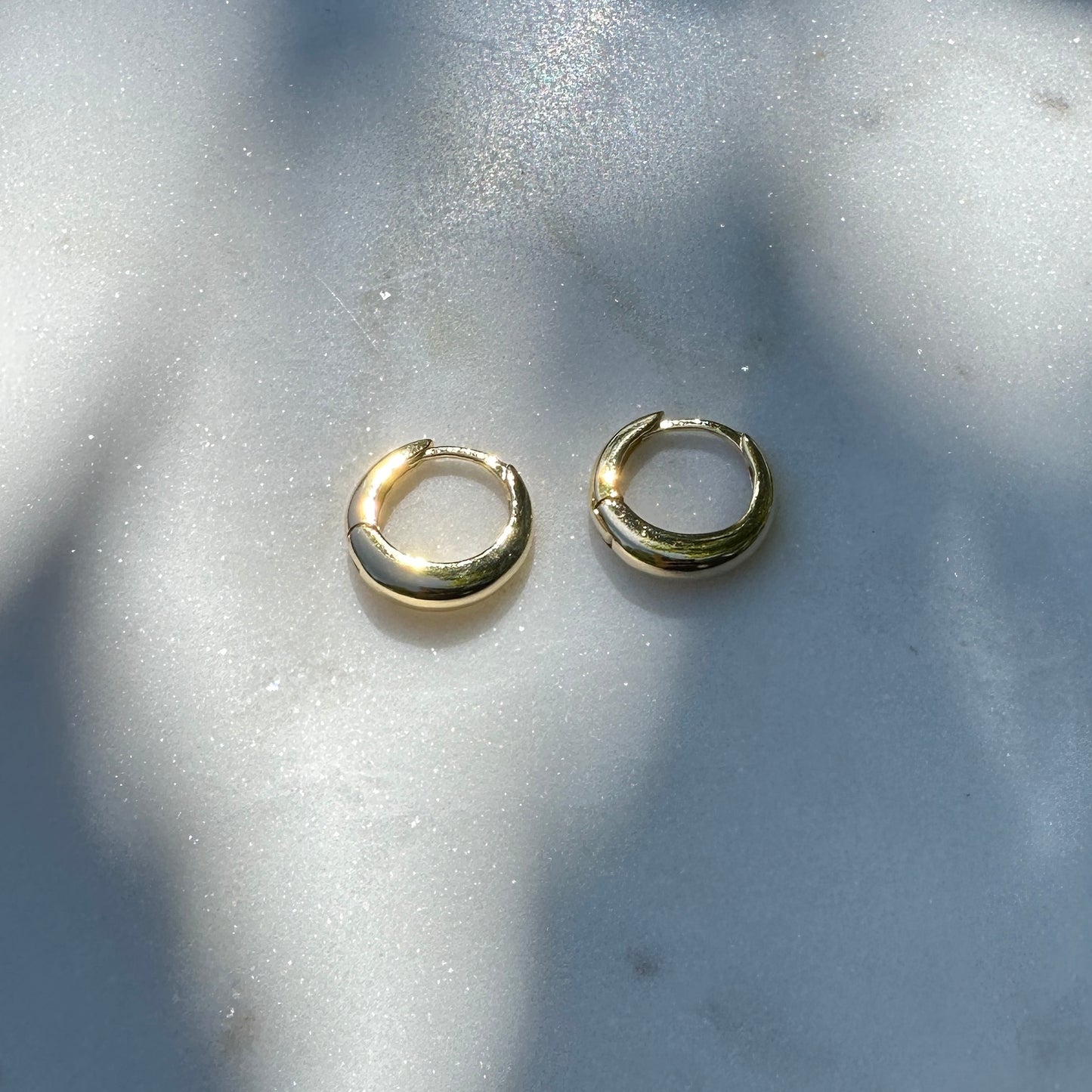 A pair of the 18K Gold Filled Classic Clicker Hoop Earrings on white marble surface from above angle with natural light