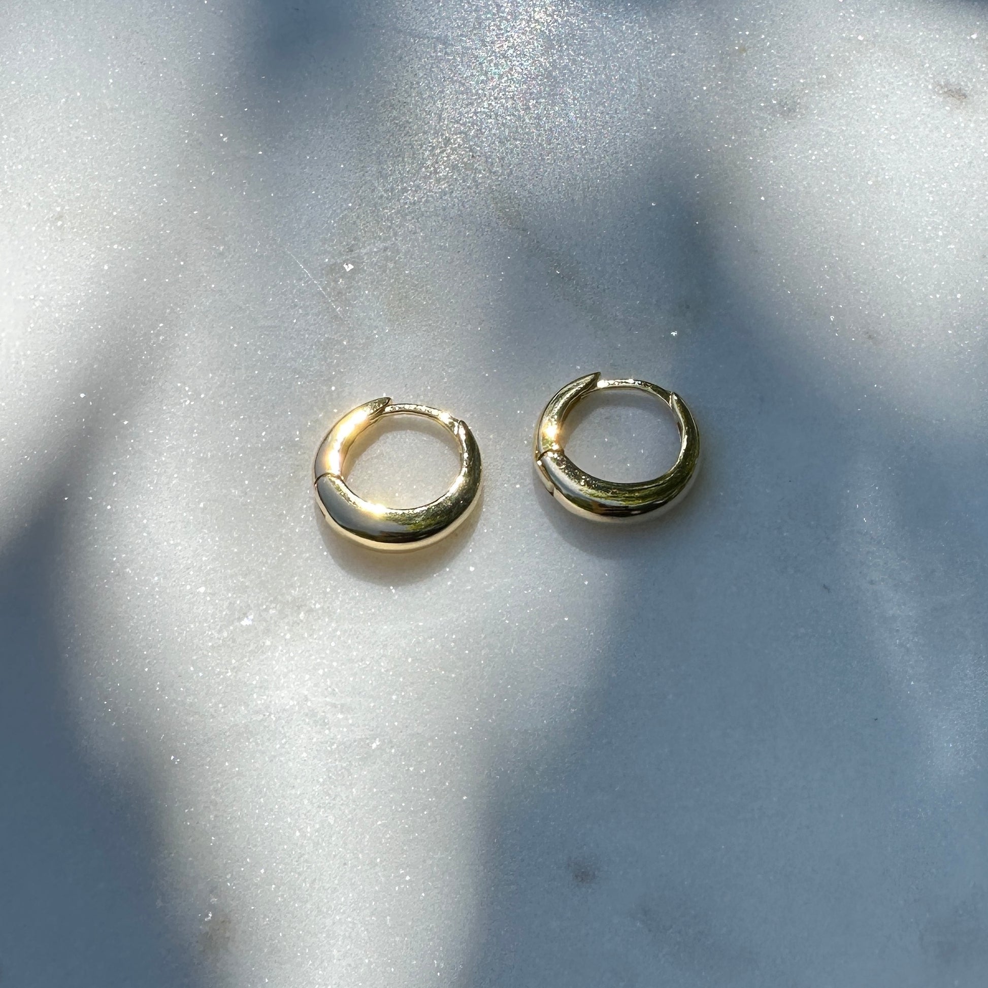 A pair of the 18K Gold Filled Classic Clicker Hoop Earrings on white marble surface from above angle with natural light
