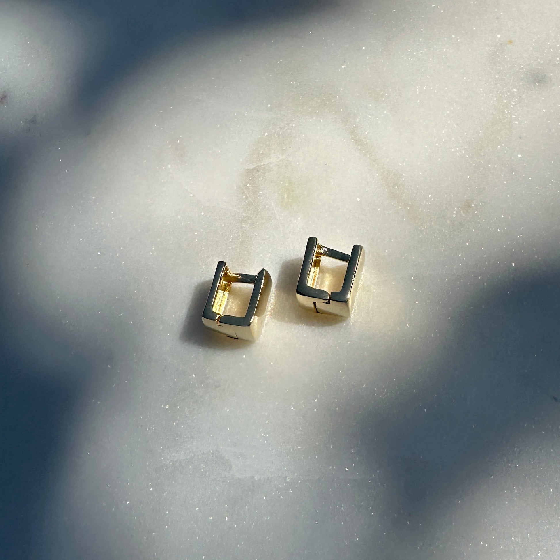 A close up image of the 18K Gold Filled Cube Clicker Earrings from an above side angle displayed on sparking marble surface 