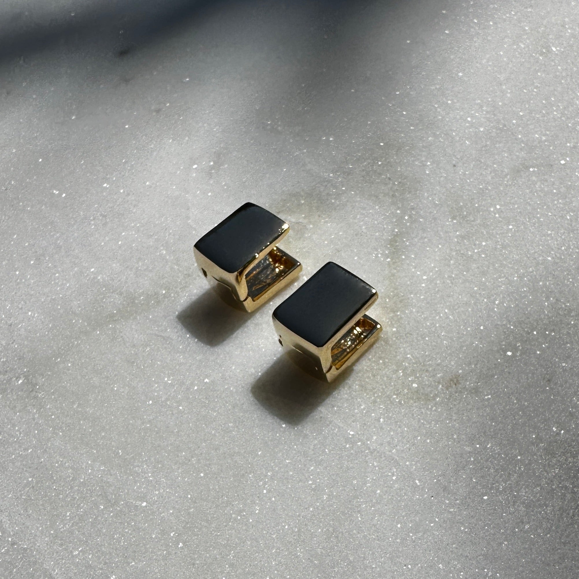 A close up image of the 18K Gold Filled Cube Clicker Earrings displayed on sparking marble surface