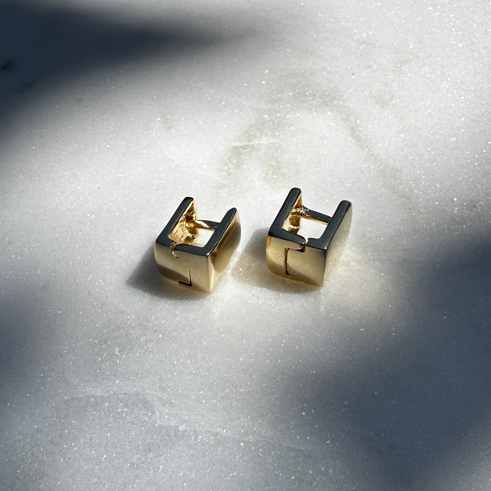 A close up image of the 18K Gold Filled Cube Clicker Earrings from a side angle displayed on sparking marble surface 