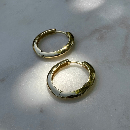 A pair of the 18K Gold Filled Lustrous Clicker Hoop Earrings on a marble surface