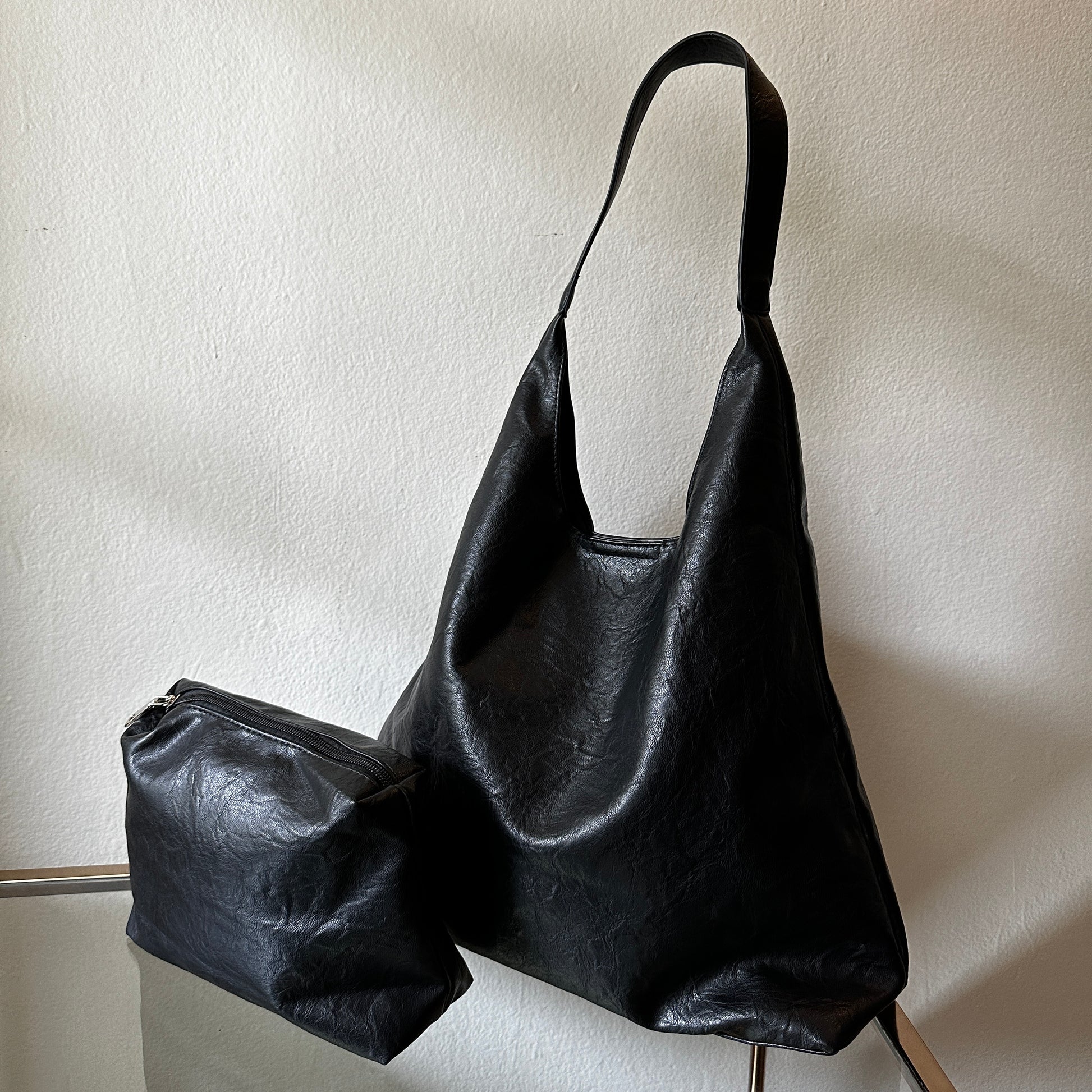 The Black Vegan Leather Shoulder Handbag and Cosmetic Pouch displayed on glass table