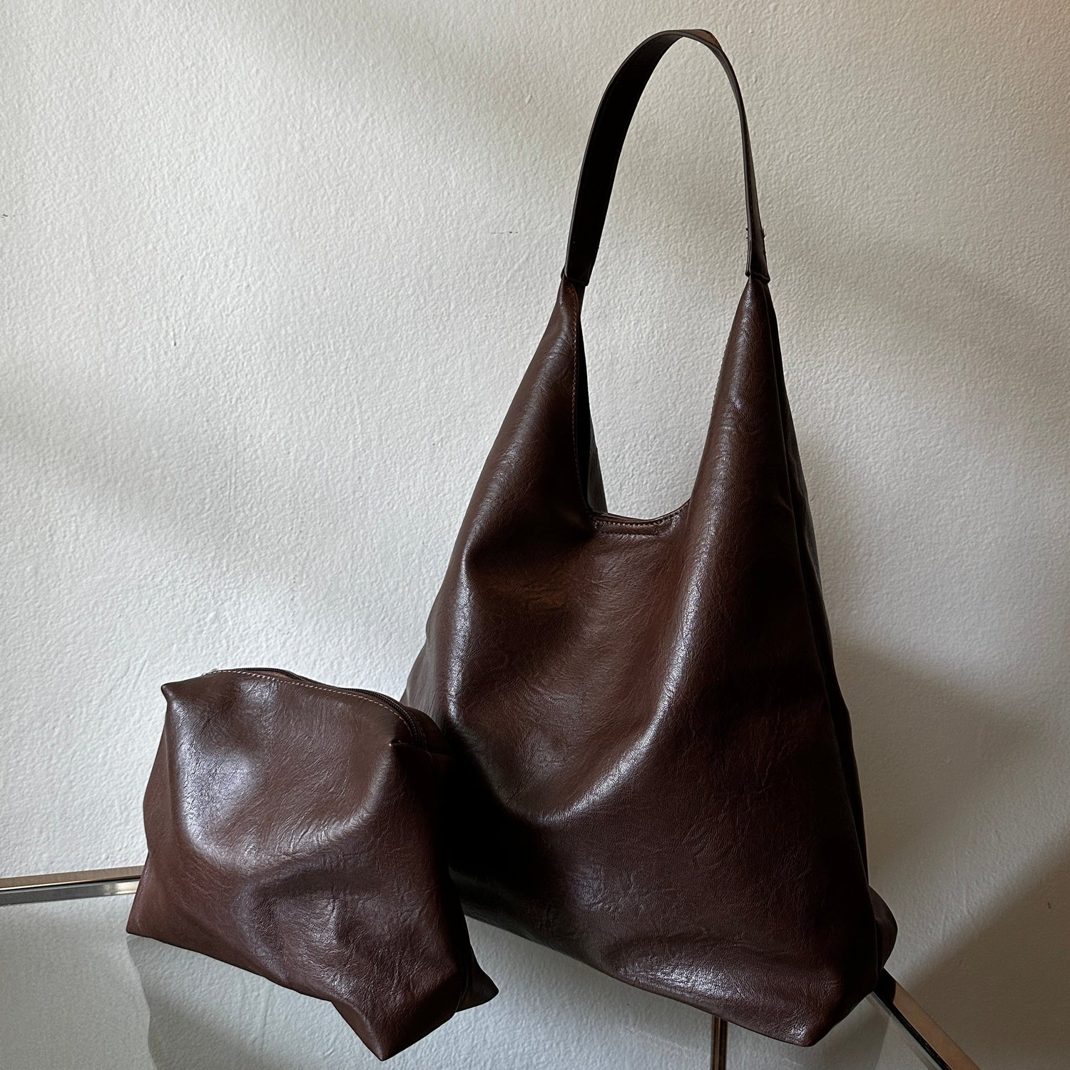 The Brown Vegan Leather Shoulder Handbag and Cosmetic Pouch displayed glass table