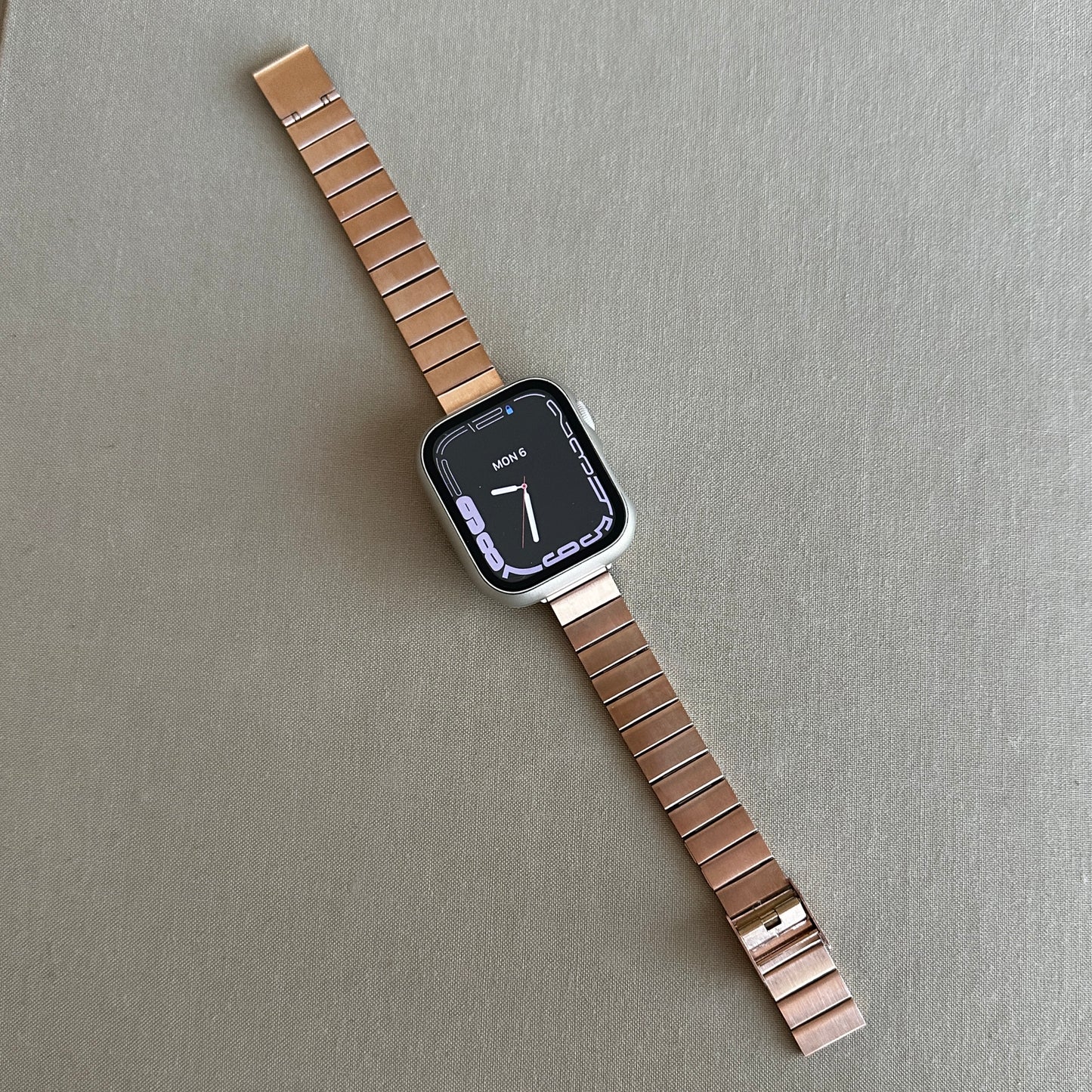 The Gold-Tone Stainless Steel Sleek Watch Band Compatible with Apple Watch displayed flat across a beige surface