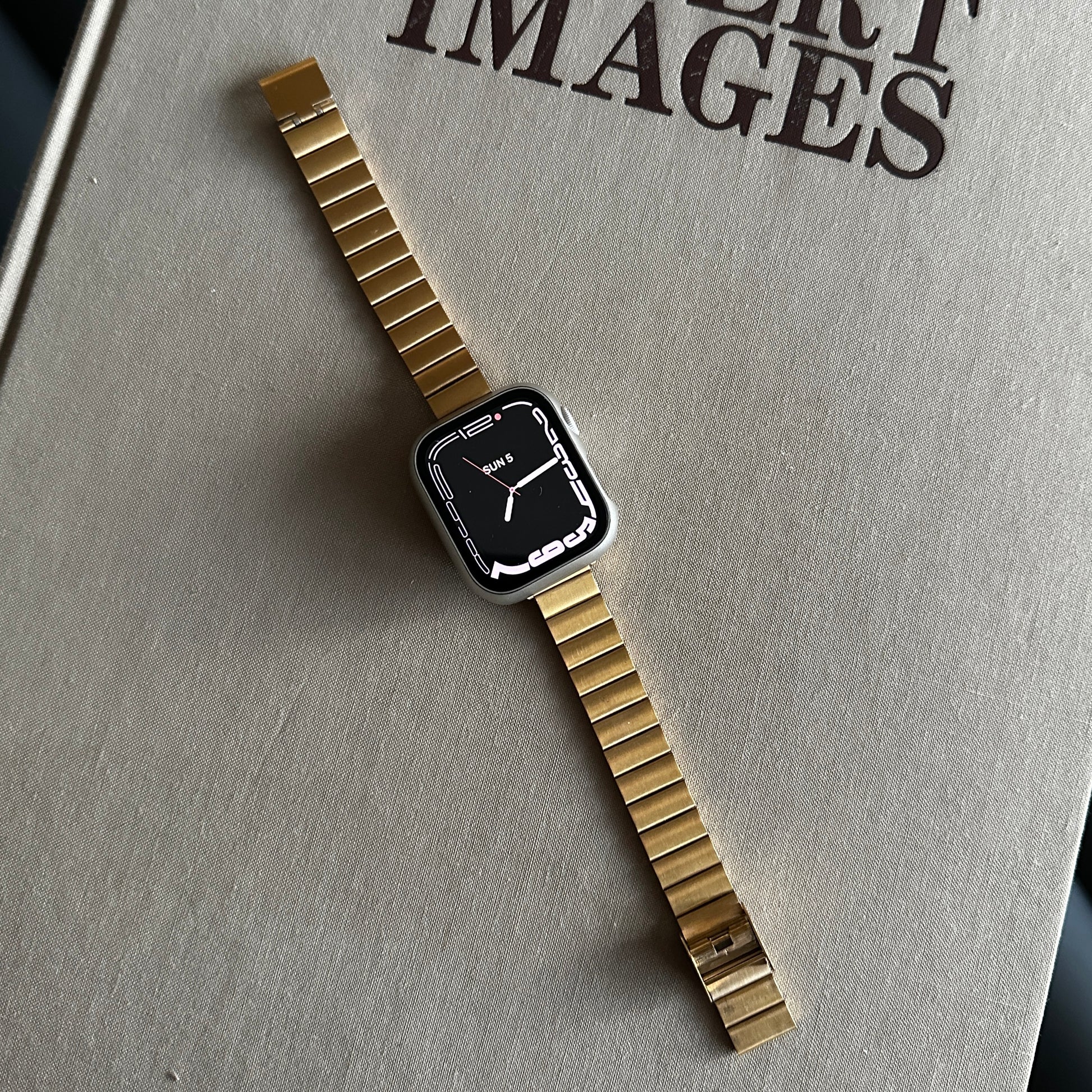 The Gold-Tone Stainless Steel Sleek Watch Band Compatible with Apple Watch displayed on a large beige surface