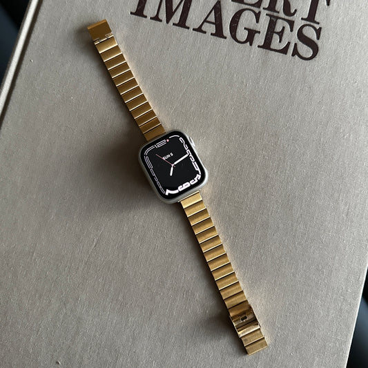 The Gold-Tone Stainless Steel Sleek Watch Band Compatible with Apple Watch displayed on a large beige surface