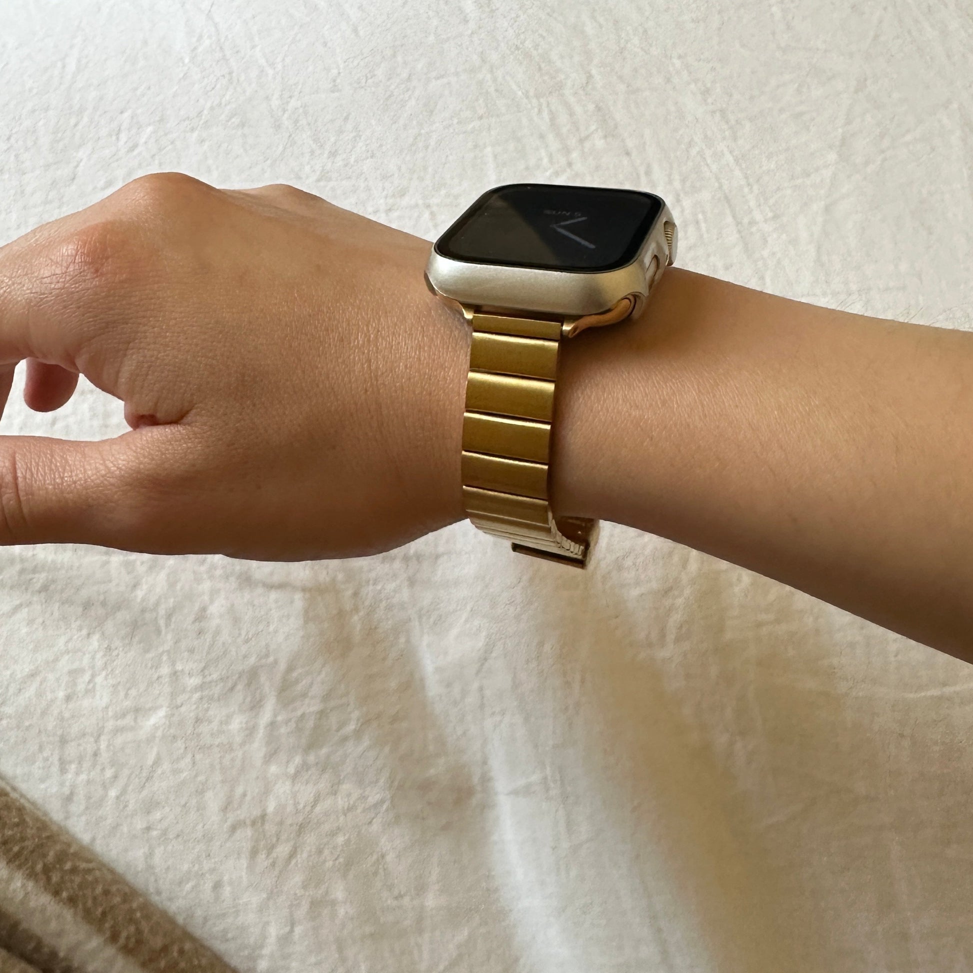 Close up image of the Gold-Tone Stainless Steel Sleek Watch Band Compatible with Apple Watch worn on female models wrist from side angle